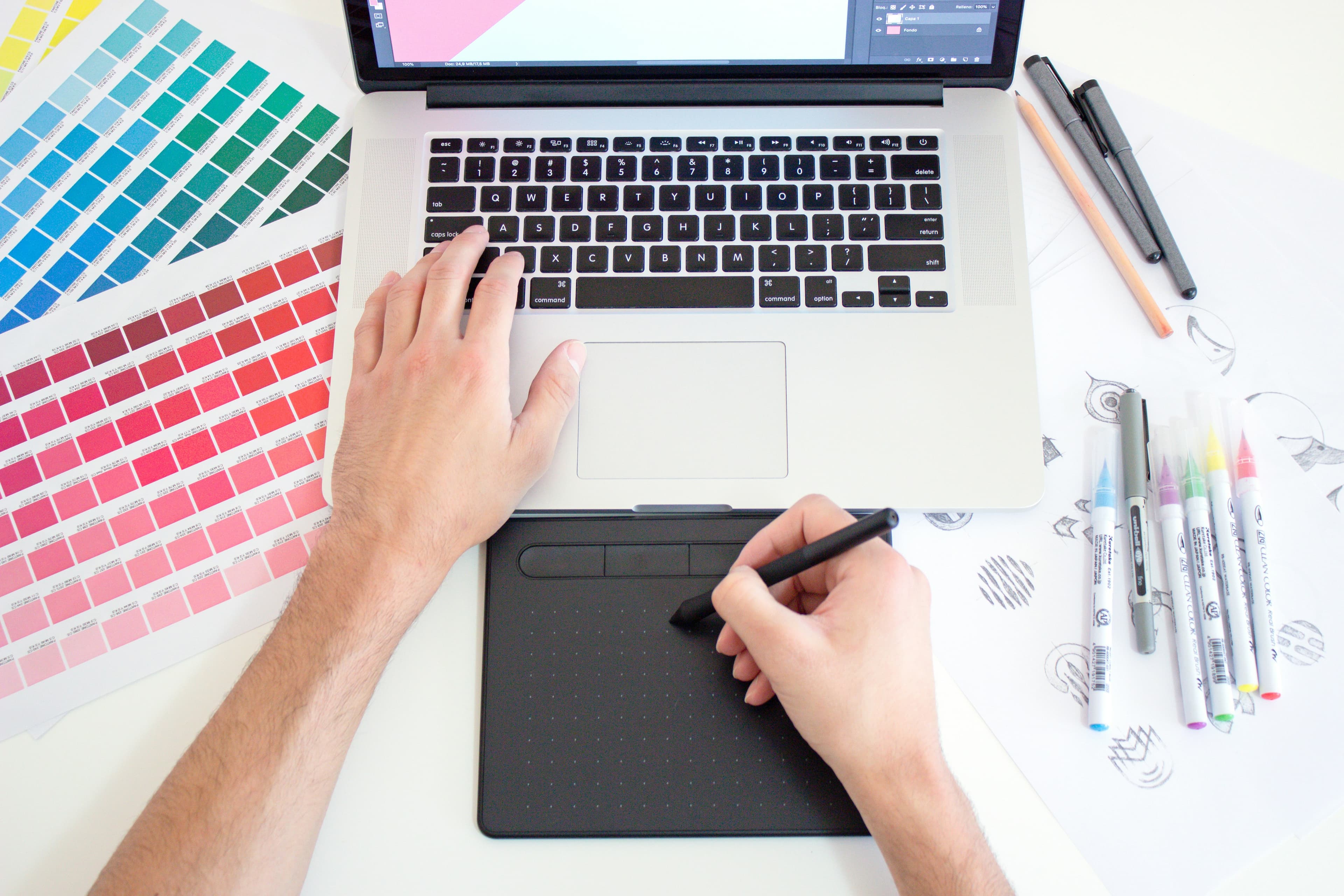 Dettaglio mani con campionari colore e tavoletta grafica accanto al laptop